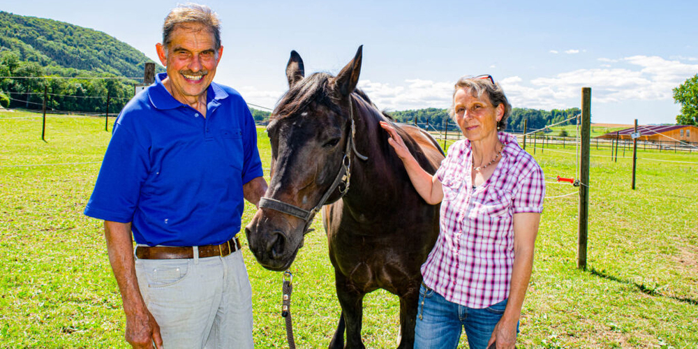 Bernhard und Daniela Neukomm stehen mit einem ihrer Pferde auf der Weide. Gemeinsam bieten sie einen Reitbetrieb an, der auch von Jung und Alt aus entfernter Umgebung besucht wird. Die Ambition, weiterzumachen, zeigt ihre Leidenschaft für Tier und Kind. 