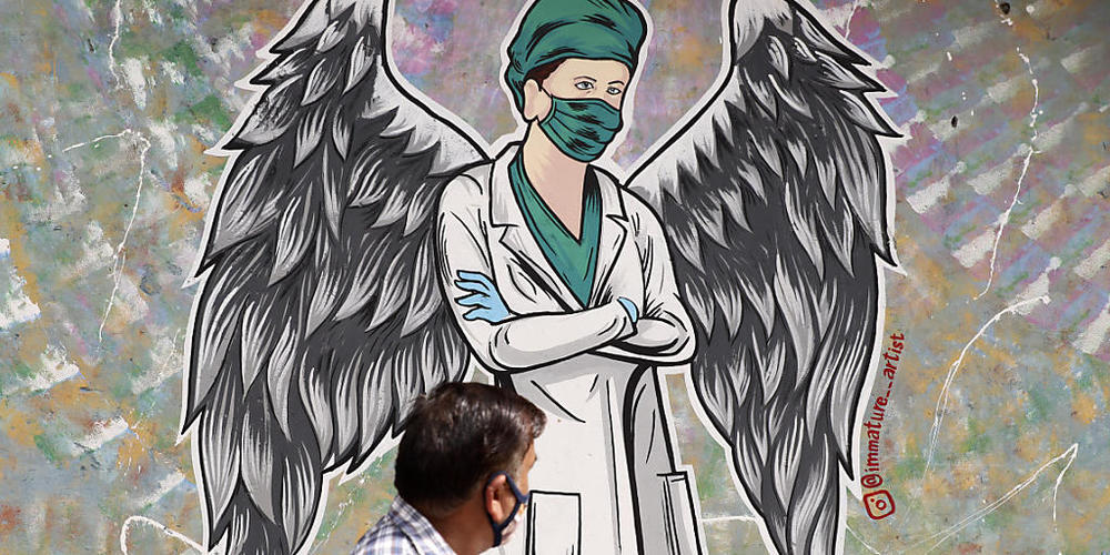 Ein Mann geht in Neu-Delhi  an einem Wandgemälde vorbei, das einen Mitarbeiter im Gesundheitswesen mit Flügeln zeigt. Indien hat heute einen neuen Tageshöchstwert an Todesfällen im Zusammenhang mit dem Coronavirus gemeldet. Foto: Amit Sharma/AP/dpa