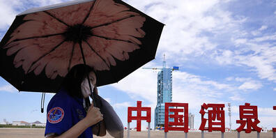 Ein Arbeiter hält einen Regenschirm in der Nähe des Raumschiffs Shenzhou-12, das auf der Startrampe mit den chinesischen Schriftzeichen "China Jiuquan Satellite Launch Center" steht. Foto: Ng Han Guan/AP/dpa