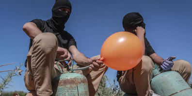 Maskierte Palästinenser füllen in einem Gebiet östlich von Gaza-Stadt Ballons mit Kühlgas, die dann mit Brandsätzen und brennbarem Material versehen werden und vom Wind in israelisches Gebiet getragen werden sollen. Foto: Mohammed Talatene/dpa