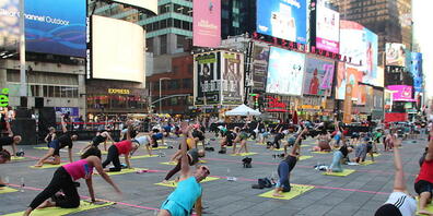 Menschen nehmen an einer gemeinsamen Yoga-Stunde inmitten des Times Square teil. Foto: Christina Horsten/dpa