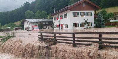 Wasser fließt über einen Platz vor einem Haus. im oberbayerischen Landkreis Berchtesgadener Land. Foto: Kilian Pfeiffer/dpa