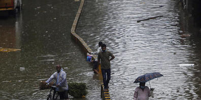 Menschen bahnen sich in Mumbai ihren Weg durch eine überschwemmte Straße nach starken Regenfällen. Foto: Rajanish Kakade/AP/dpa