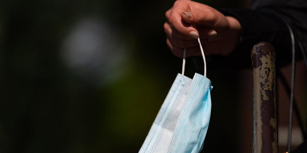 ARCHIV - Eine Frau hält einen Mundschutz in der Hand. Angesichts steigender Corona-Zahlen führt Island wieder Beschränkungen im öffentlichen Leben ein. Unter anderem sollen die Isländer wieder mindestens einen Meter Abstand halten und in Innenräum...