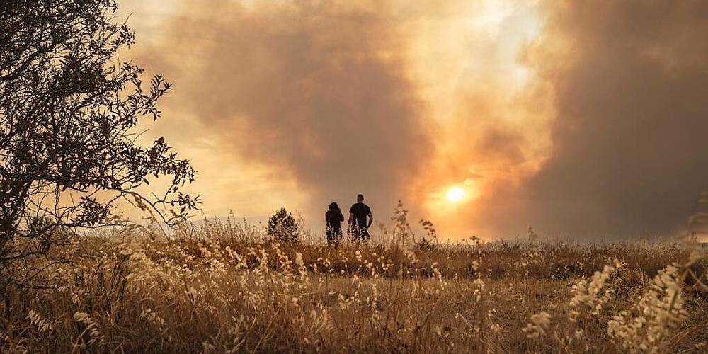 Menschen beobachten einen Waldbrand in Südfrankreich. Im Kampf gegen den Brand zwischen den Städten Narbonne und Carcassonne sind über 1000 Feuerwehrleute und Retter im Einsatz. Foto: Idriss Bigou-Gilles/AFP/dpa