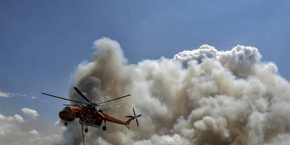 Ein Löschhubschrauber fliegt während eines Waldbrandes über einen Wasserspeichertank. Foto: Valerie Gache/AP/dpa