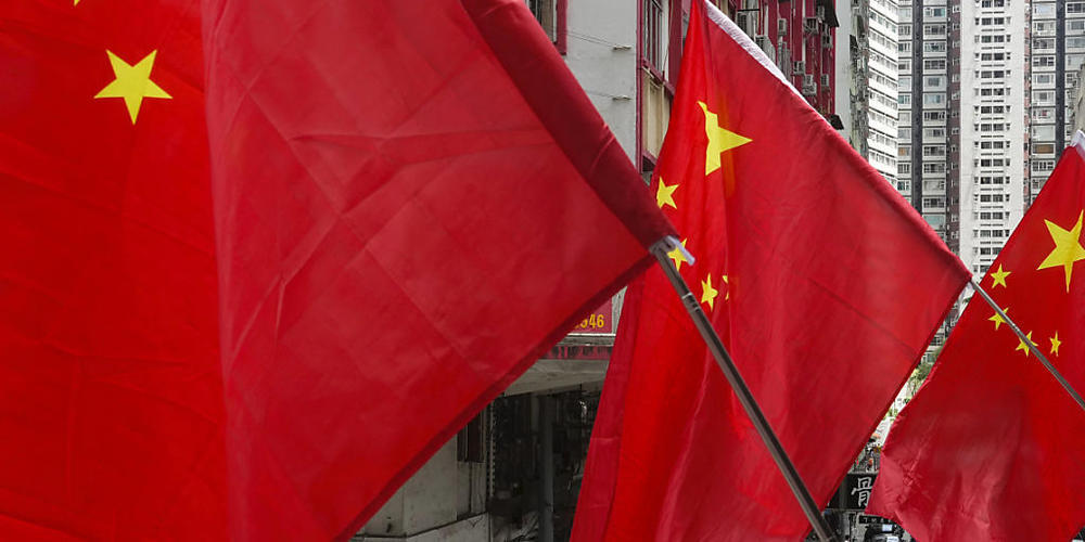 Menschen laufen unter chinesischen Flaggen, die als Teil einer Flaggenzeremonie aufgestellt wurden. Foto: Vincent Yu/AP/dpa/Symbolbild