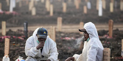 dpatopbilder - Mitarbeiter des Rorotan-Friedhof in Jakarta, welcher für Corona-Tote reserviert ist, tragen Schutzkleidung und sitzen während einer Pause zwischen den Gräbern. Foto: Dita Alangkara/AP/dpa