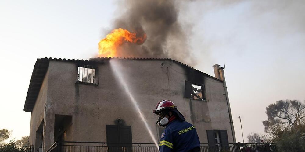 Ein Feuerwehrmann löscht einen Brand an einem Gebäude, der durch das Feuer von Waldbrände entfacht ist. Feuerwehrleute in Griechenland kämpfen auch am Mittwochmorgen weiter gegen den Großbrand in den nördlichen Vorstädten Athens. Regierungschef Ky...