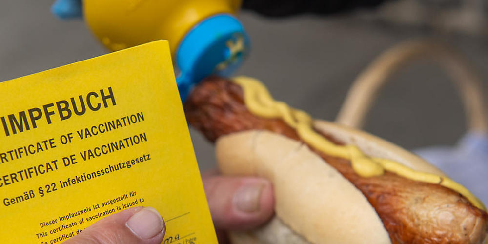 Ein Mann hält am mobilen Impfzentrum in Aue seinen Impfpass und eine Bratwurst im Bötchen. Für die zweitägige Impfaktion hat sich die Stadt etwas besonderes ausgedacht. Nach erfolgreicher Impfung mit dem Impfstoff von Biontech/Pfizer erhalten die ...