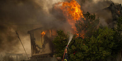 Feuerwehrleute versuchen einen Waldbrand in einem Waldgebiet nördlich von Athen zu löschen.  Seit den frühen Morgenstunden fachten starke Westwinde am Freitag die zahlreichen Feuer weiter an. Foto: Angelos Tzortzinis/dpa