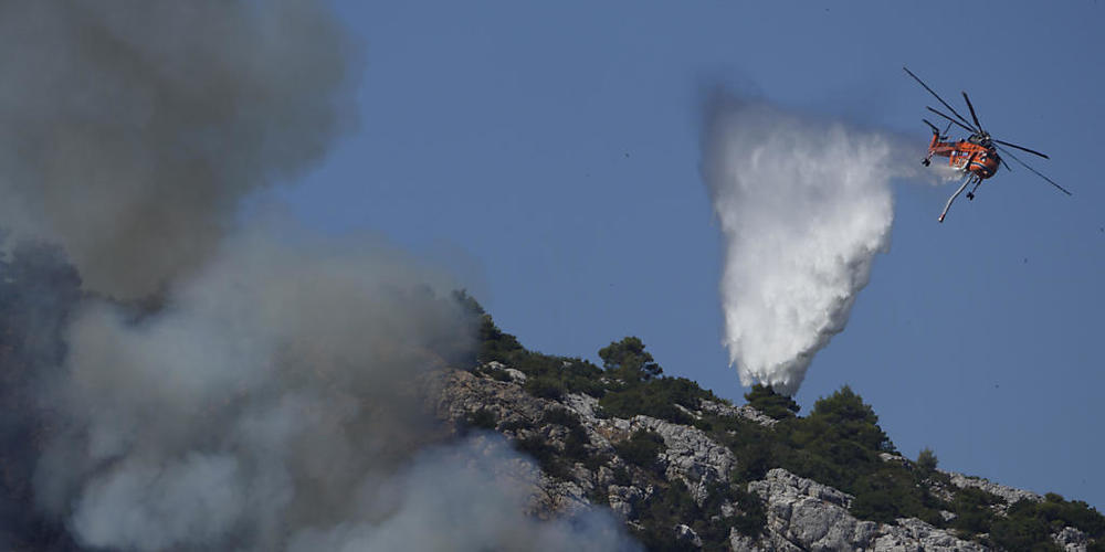 Ein Hubschrauber wirft über einem Feuer in der Nähe des Dorfes Malakasa nördlich von Athen Wasser ab. Foto: Petros Karadjias/AP/dpa