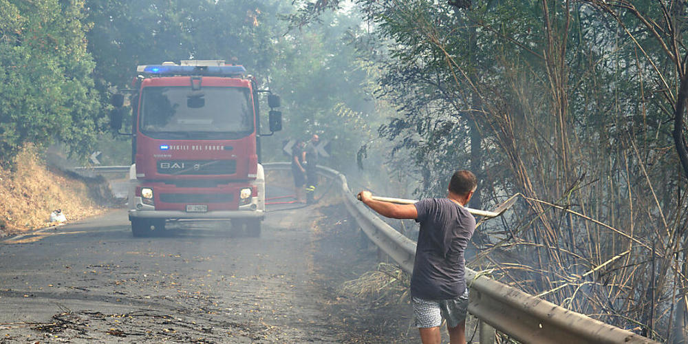 Ein Mann gestikuliert in Richtung Feuerwehr, die mit einem Löschzug eine Straße entlang fährt. Foto: Luigi Salsini/LaPresse via ZUMA Press/dpa