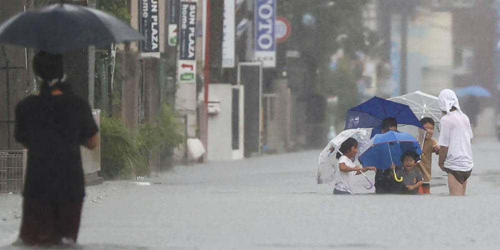 Menschen waten durch eine überflutete Straße in Kurume, Westjapan. Sintflutartige Regenfälle suchten den Südwesten Japans seit Freitag heim und forderten mindestens sechs Todesopfer. Nach einer Unterbrechung regnete es am Montagmorgen (Ortszeit) a...