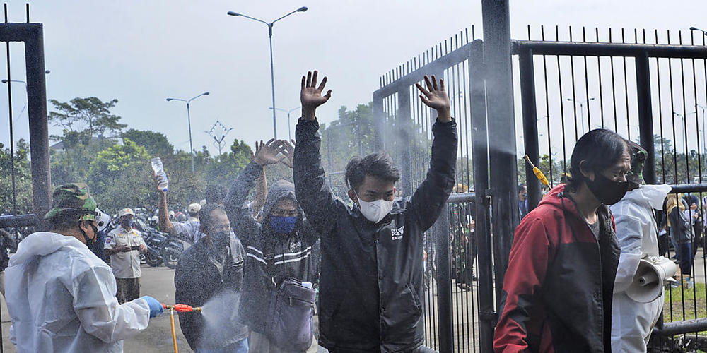 Soldaten in Schutzanzügen sprühen Desinfektionsmittel auf Menschen, die das Stadion Gelora Bandung Lautan Api Stadion betreten, um gegen den Coronavirus impfen zu lassen. Foto: Bukbis Candra/AP/dpa