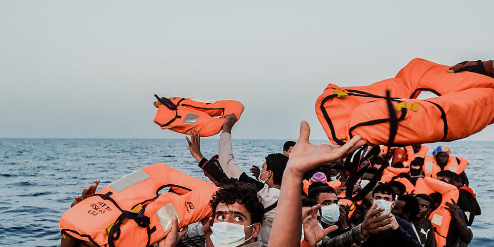 HANDOUT - Ein Helfer reicht den Bootsmigranten in einem kleinen Boot Rettungswesten. Foto: Flavio Gasperini/SOS Mediterranee/dpa - ACHTUNG: Nur zur redaktionellen Verwendung im Zusammenhang mit der aktuellen Berichterstattung und nur mit vollständ...