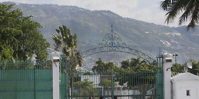 Fußgänger gehen am Tor des Präsidentenpalast vorbei. Präsident Moise war in der Nacht zum Mittwoch gegen 1.00 Uhr (Ortszeit) in seiner Residenz erschossen worden. Trotz erster Festnahmen ist die Lage in Haiti weiterhin angespannt. Foto: Joseph Ode...
