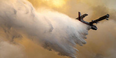 Ein Löschflugzeug wirft Wasser auf einen brennenden Bergrücken ab, wo eine Feuerlinie von Mannschaften der Waldbrandbekämpfung geschaffen wurde. Foto: Pete Caster/Lewiston Tribune via AP/dpa - ACHTUNG: Nur zur redaktionellen Verwendung und nur mit...