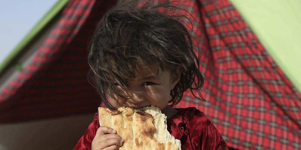 Ein afghanisches Mädchen, das aufgrund von von Kämpfen zwischen den Taliban und afghanischen Sicherheitskräften aus ihrer Heimat geflohen ist, steht vor einem Zelt in Masar-e Scharif und isst Brot. Foto: Rahmat Gul/AP/dpa