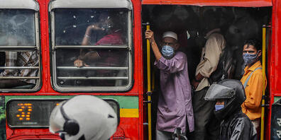 Personen tragen Mund-Nasen-Schutz, als sie in einem voll besetzten Bus fahren. Foto: Rafiq Maqbool/AP/dpa