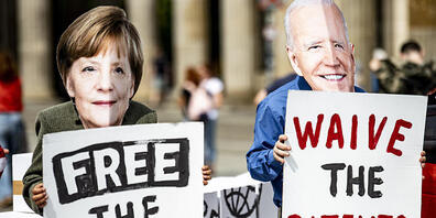 Aktivisten mit Masken, die Bundeskanzlerin Merkel und den US-Präsidenten Biden darstellen, stehen vor dem Brandenburger Tor in Berlin. Die Aktivisten fordern die vorübergehende Aussetzung des Patentschutzes für die Covid-Impfstoffe. Foto: Fabian S...