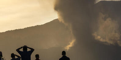 Anwohner blicken von einem Hügel aus auf die Lava, die weiterhin aus einem ausgebrochenen Vulkan auf der Insel La Palma fließt. Foto: Emilio Morenatti/AP/dpa