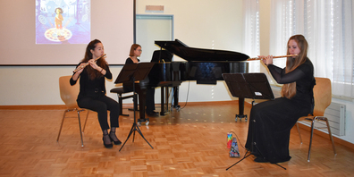 Die drei Musikerinnen während des Auftritts, auf der Leinwand im Hintergrund die Bilder zur Geschichte. 
