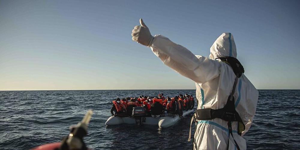 ARCHIV - Ein Mitarbeiter NGO «Open Arms» vor der libyschen Küste gestikuliert in Richtung eines überfüllten Schlauchbootes, auf dem sich Migranten aus verschiedenen afrikanischen Ländern befinden (Bild vom 06.02.). Hilfsorganisationen fahren immer...