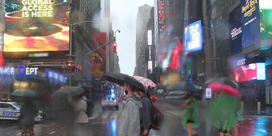 Fußgängerinnen und Fußgänger bei der Straßenüberquerung am Times Square schützen sich mit Regenschirmen vor starkem Regen. Der Tropensturm «Henri» hat in der U-Bahnstation Times Square - 42nd Street einen Wasserschaden verursacht. Foto: Niyi Fote/...