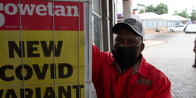 Ein Tankwart steht neben einer Zeitungsschlagzeile mit dem Titel «New covid variant here» (dt. Neue Covid-Variante hier). Die Omikron-Variante(B.1.1.529) war zuerst im südlichen Afrika nachgewiesen worden. Die Weltgesundheitsorganisation (WHO) stu...