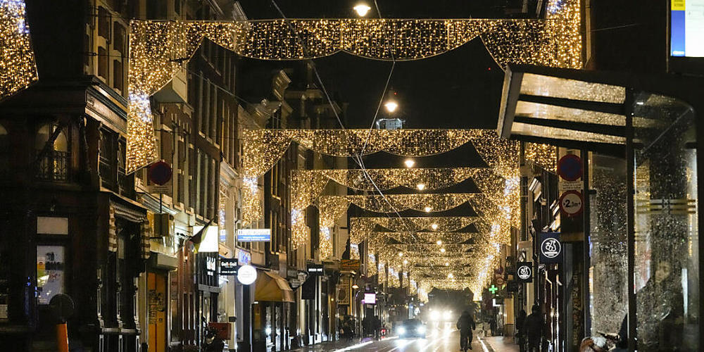 Eine Frau wartet in Amsterdam auf eine Straßenbahn in einer nahezu menschenleeren Straße. Angesichts schnell steigender Infektions- und Patientenzahlen verhängen die Niederlande einen abendlichen Lockdown. Foto: Peter Dejong/AP/dpa