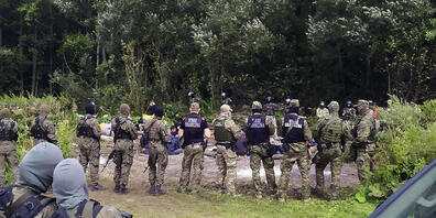 ARCHIV - Migranten sitzen nach dem Grenzübertritt von Belarus nach Polen hinter Sicherheitskräften. Seit Monaten ist die Situation an der polnisch-belarussischen Grenze angespannt. Foto: Mateusz Wodzinski/AP/dpa