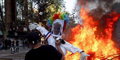 Ein Demonstrant hält ein Puppe mit einem Foto des chilenischen Präsidenten Pinera bei einem Feuer. Foto: Luis Hidalgo/AP/dpa