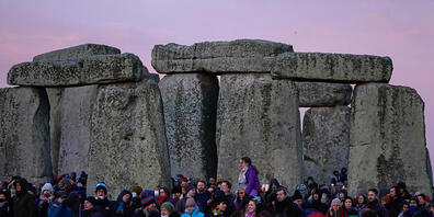 Einige Menschen sind am prähistorischen Monument von Stonehenge auf der Salisbury Plain versammelt, um an den Feierlichkeiten zur Wintersonnenwende teilzunehmen. Foto: Andrew Matthews/PA Wire/dpa
