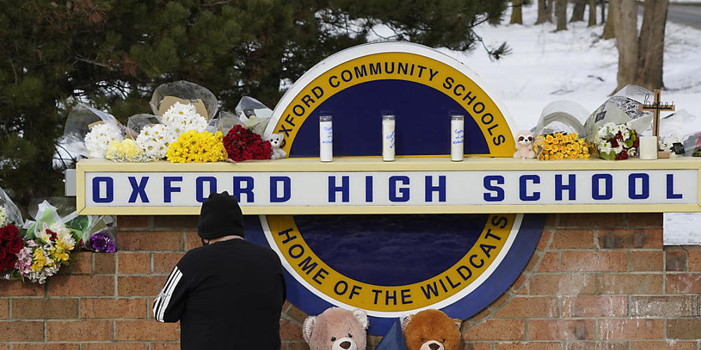 Eine Frau kniet zum Gebet vor dem Schild der Oxford High School in Michigan. Foto: Paul Sancya/AP/dpa