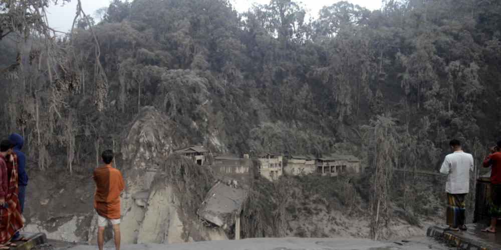 Dorfbewohner stehen vor einem Hang an der eine Brücke durch den Lavastrom, bei Ausbruch des Mount Semeru, zerstört wurde. Foto: Hendra Permana/AP/dpa
