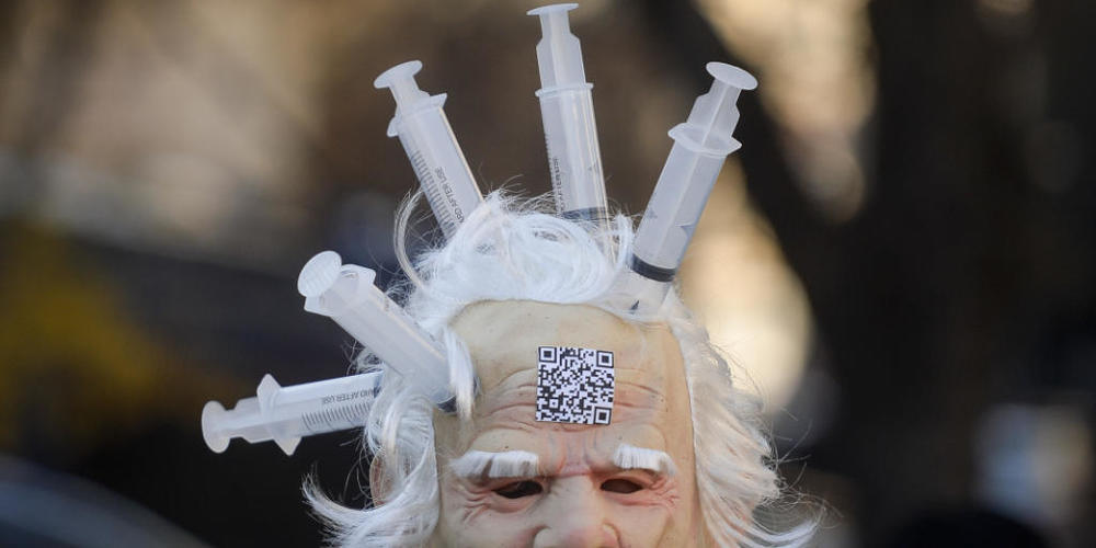 Eine Person trägt eine Latexmaske, an der Spritzen befestigt sind. In Bukarest wird gegen Impfungen, die Einführung des «Grünen Passes» und Einschränkungen in Bezug auf das Coronavirus demonstriert. Foto: Alexandru Dobre/AP/dpa