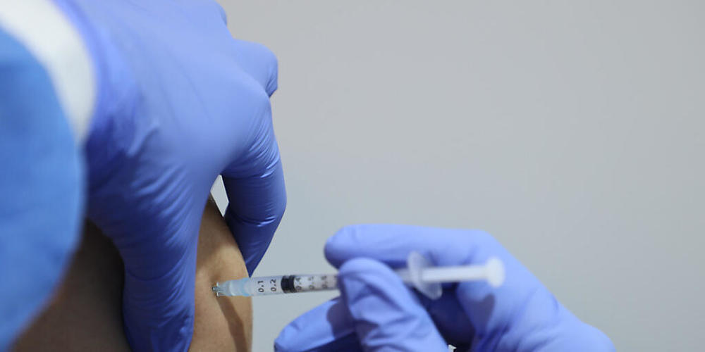 Ein medizinischer Mitarbeiter impft einen Mann mit dem Impfstoff von Biontech.