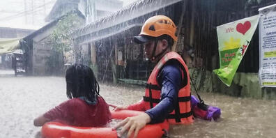 HANDOUT - Dieses von der philippinischen Küstenwache zur Verfügung gestellte Foto zeigt eine Rettungskraft die ein Mädchen durch das Hochwasser evakuiert. Foto: Uncredited/Philippine Coast Guard/dpa - ACHTUNG: Nur zur redaktionellen Verwendung und...