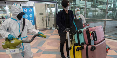 ARCHIV - Ein Flughafenmitarbeiter desinfiziert das Gepäck eines ausländischen Reisenden nach seiner Ankunft am Suvarnabhumi International Airport. Wegen der Ausbreitung Omikron-Variante des Coronavirus wollen Behörden in Thailand in dieser Woche p...