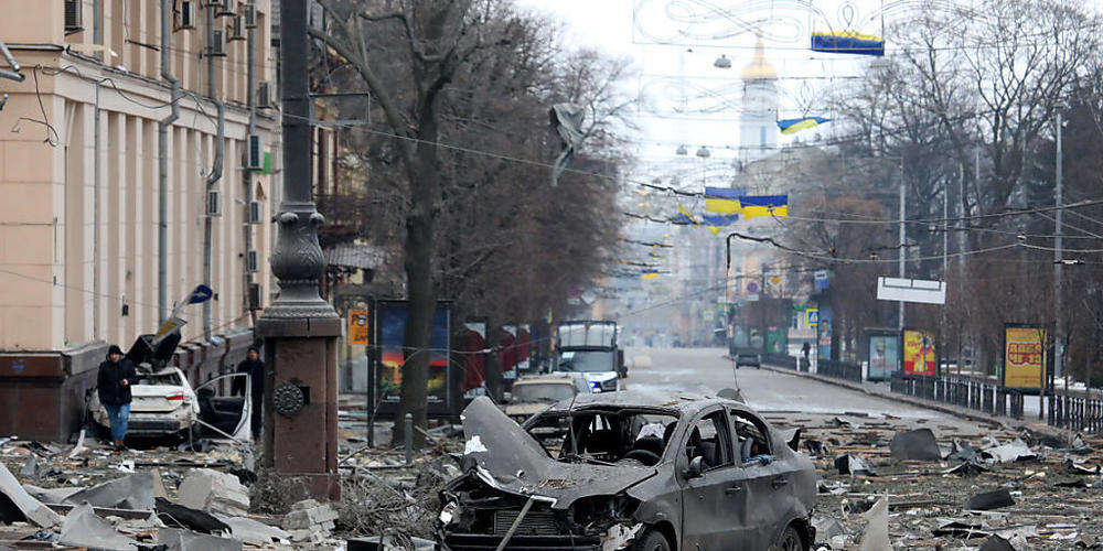 Ein ausgebranntes Autos steht auf der Straße in der Nähe des durch Angriffe zerstörten Gebäudes der regionalen Verwaltung von Charkiw. Foto: ---/Ukrinform/dpa
