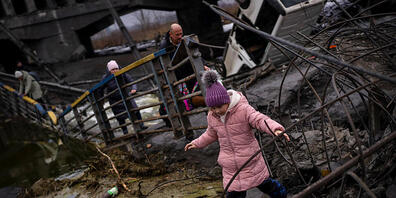 Ein Mädchen flieht mit seiner Familie über eine zerstörte Brücke am Rande von Kiew. Die russischen Streitkräfte haben ihre Angriffe auf belebte Städte ausgeweitet, was der ukrainische Staatschef als unverhohlene Terrorkampagne bezeichnet. Foto: Em...