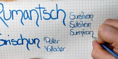 Eine Primarschülerin notiert sich die verschiedenen Idiome neben der romanischen Schriftsprache Rumantsch Grischun. Der Bund will die vierte Landessprache im Unterricht stärker fördern. (Archivbild)