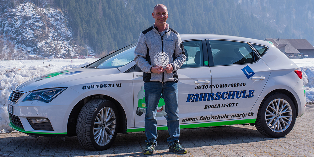 Roger Marty zeigt seine Auszeichnung zum besten Fahrlehrer des Kantons Schwyz 2022. Mit seinem Seat Leon ist er sicher und erfolgreich unterwegs.
