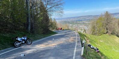 Nach einer Doppelkollision stehen zwei beschädigte Motorräder und ein demoliertes Auto auf der Bucheneggstrasse bei Adliswil.
