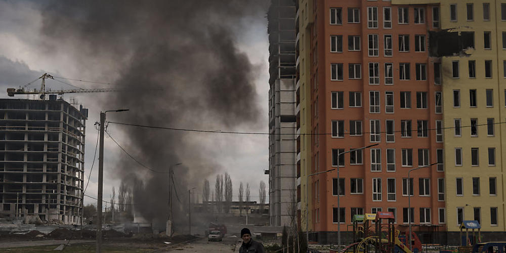 Ein Mann steht nach einem russischen Angriff auf der Straße, während im Hintergrund Rauch aufsteigt. Foto: Felipe Dana/AP/dpa