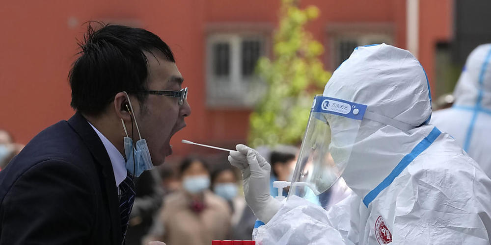 Ein Angestellter (l) öffnet den Mund für einen Coronavirus-Test vor einem Hotel im chinesischen Bezirk Haidian. Foto: Ng Han Guan/AP/dpa