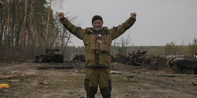 Ein ukrainischer Soldat steht auf einer Straße vor zerstörten russischen Panzern und hebt dabei die geballten Fäuste. Foto: Vadim Ghirda/AP/dpa