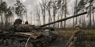 Ein ukrainischer Soldat steht am Stadtrand von Kiew neben einem zerstörten Panzer. Foto: Vadim Ghirda/AP/dpa