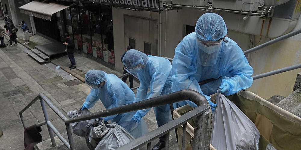 Hotelangestellte tragen Schutzkleidung und entsorgen den Müll aus einem Hotel, das zur Isolation genutzt wird. Foto: Kin Cheung/AP/dpa